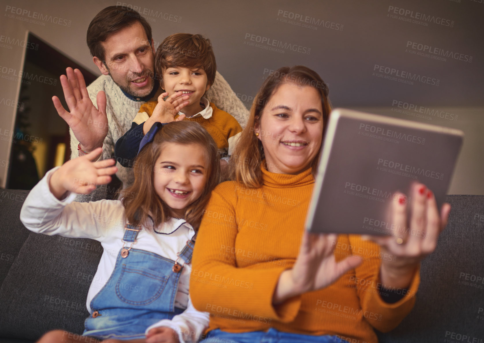 Buy stock photo Cropped shot of an affectionate young family of four video chatting using a digital tablet on the sofa at home