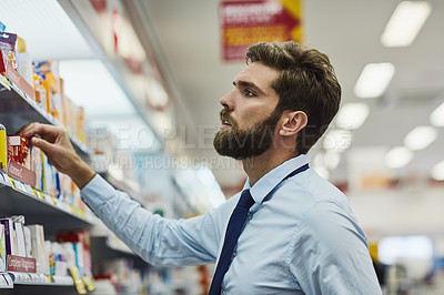 Buy stock photo Cropped shot of a handsome young man looking for medication in a pharmacy