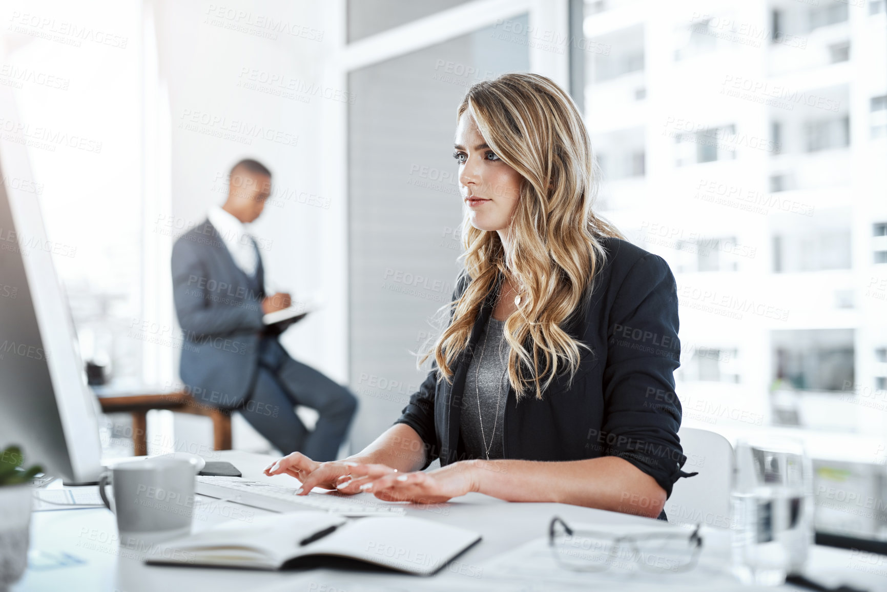 Buy stock photo Shot of a young businesswoman using a computer at her desk in a modern office