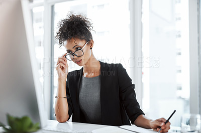 Buy stock photo Shot of a young businesswoman using a computer and writing notes at her desk in a modern office