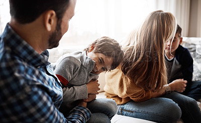 Buy stock photo Family, children and a father tickling his son in the living room of their home together with mom and brother in the background. Playful, relax or love with a man, woman and kids bonding in a house