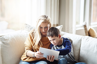 Buy stock photo Shot of an adorable little boy using a digital tablet with his mother while relaxing on the sofa at home