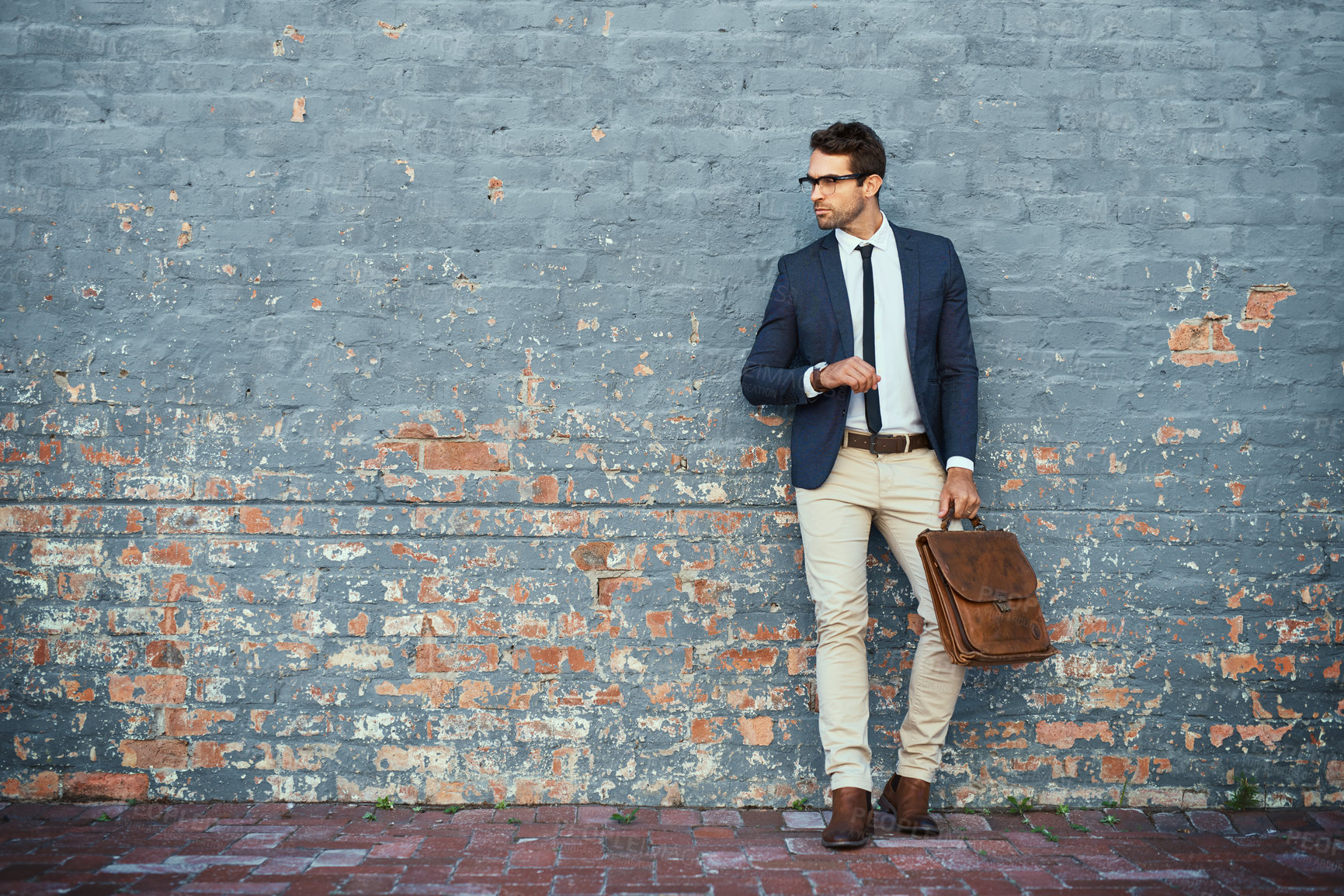 Buy stock photo Full length shot of a handsome young businessman standing against a grey facebrick wall