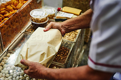 Buy stock photo Shot of an unrecognizable man packing up goods into a paper bag to give to a customer at a market during the day