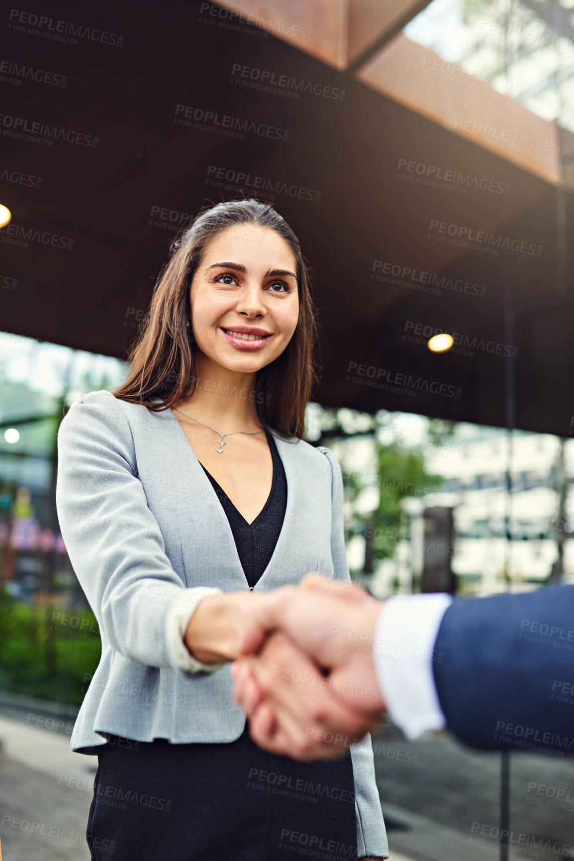 Buy stock photo Cropped shot of a beautiful young businesswoman shaking hands with an unrecognizable businessman outside