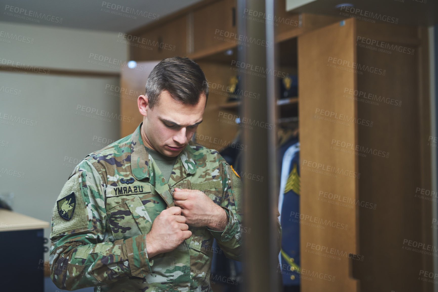 Buy stock photo Shot of a young soldier standing getting dressed in the dorms of a military academy