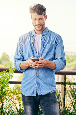 Buy stock photo Shot of a confident young man texting on his cellphone outside during the day