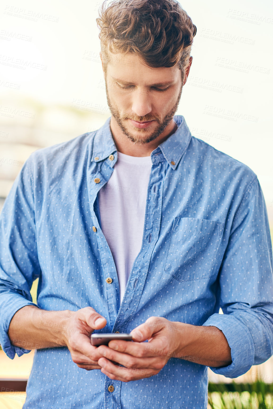 Buy stock photo Shot of a confident young man texting on his cellphone outside during the day
