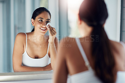 Buy stock photo Shot of a beautiful young woman cleaning her face with cotton wool in the bathroom mirror