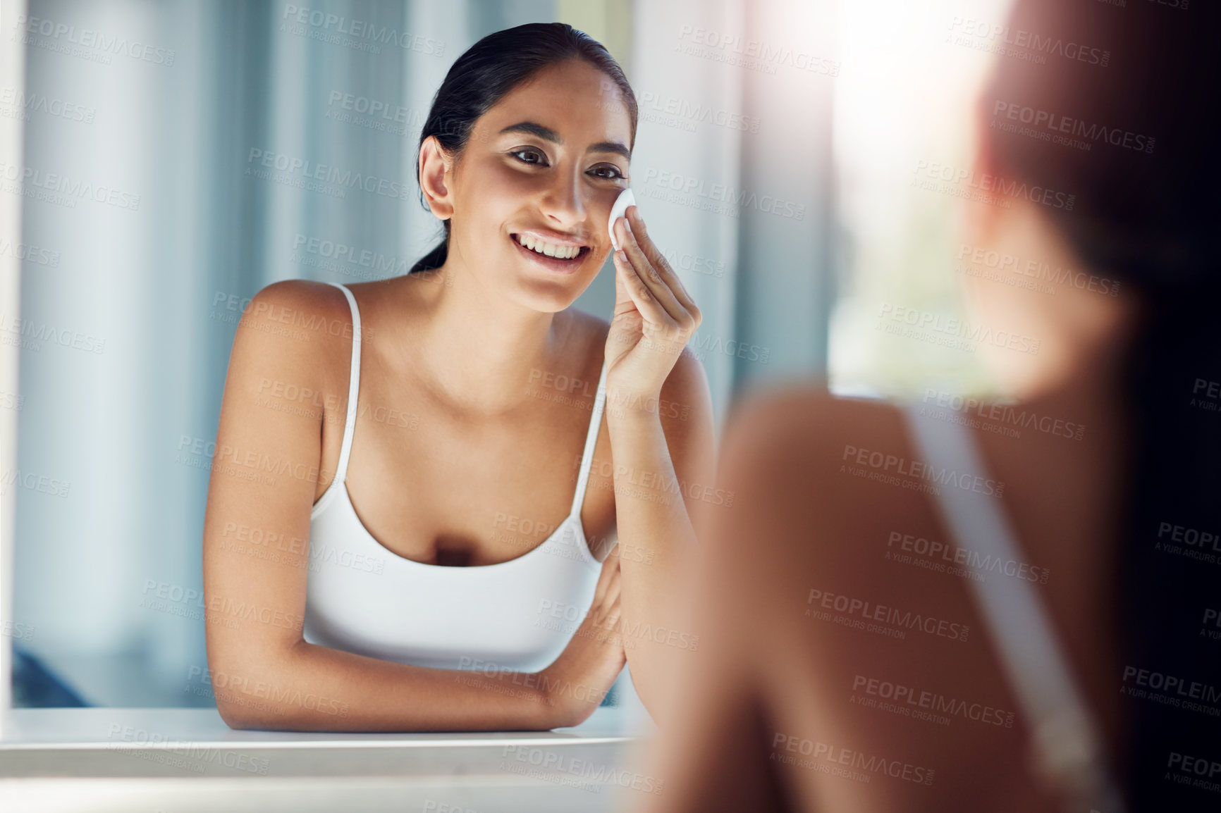 Buy stock photo Shot of a beautiful young woman cleaning her face with cotton wool in the bathroom mirror
