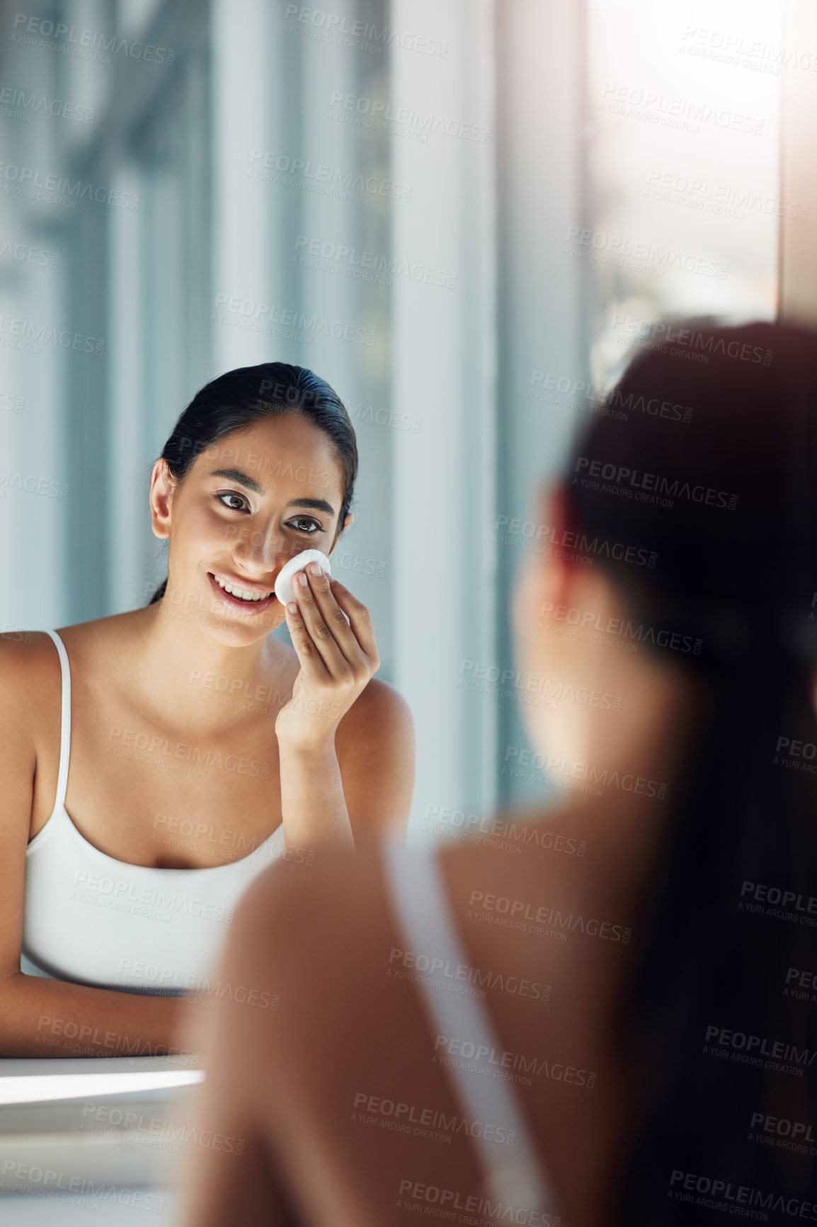 Buy stock photo Shot of a beautiful young woman cleaning her face with cotton wool in the bathroom mirror