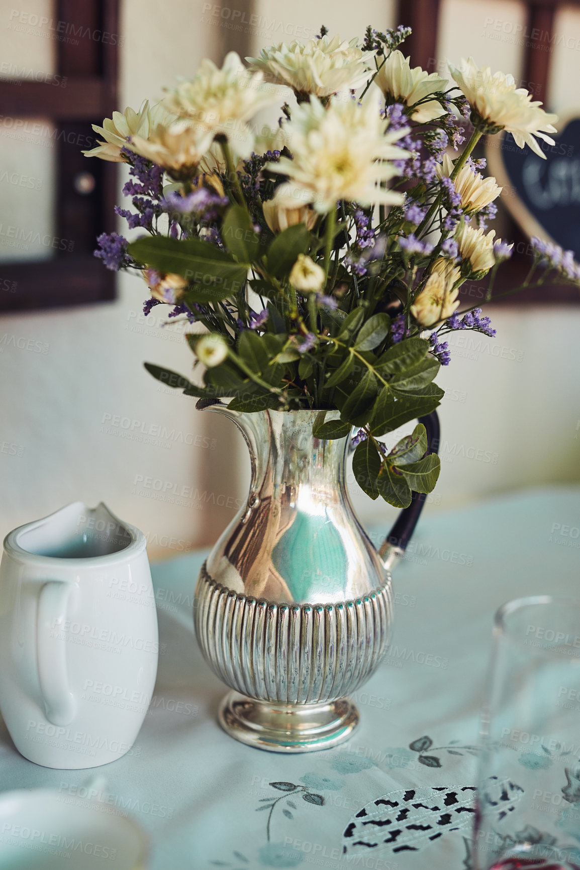 Buy stock photo Shot of a metal vase filled with flowers on a table at a tea party inside