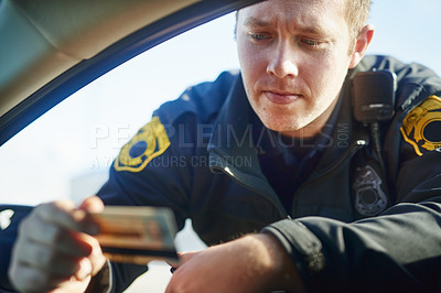 Buy stock photo Cropped shot of a handsome young male traffic officer checking a license at a roadblock