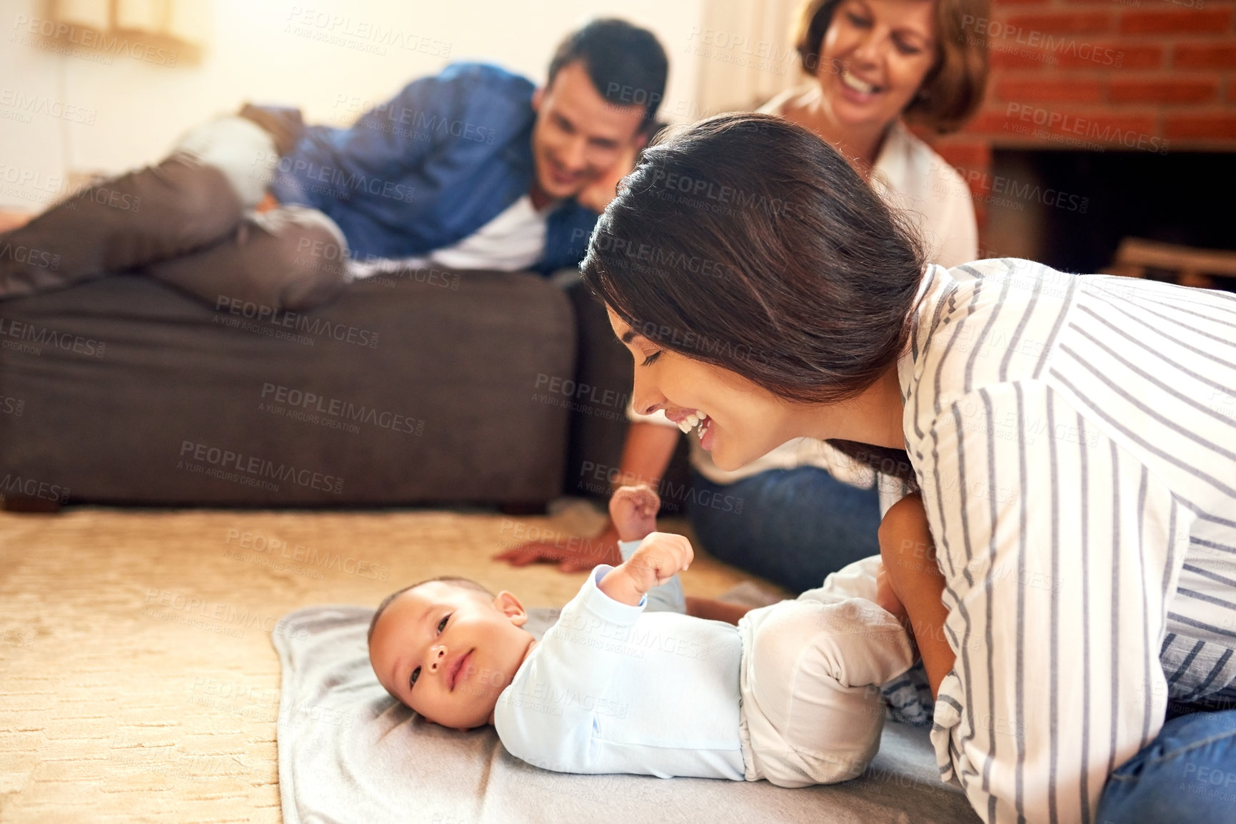 Buy stock photo Cropped shot of an attractive young woman and her baby boy bonding at home with the family in the background