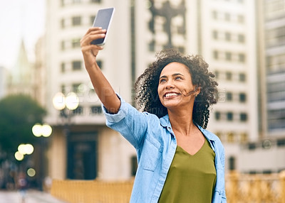 Buy stock photo Shot of a young woman taking a selfie on her cellphone while out in the city