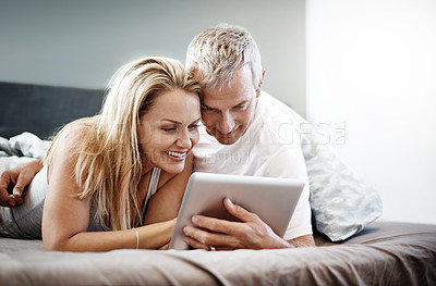 Buy stock photo Shot of a mature couple using a digital tablet while lying in bed