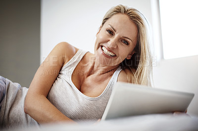 Buy stock photo Shot of a mature woman using her digital tablet while lying in bed