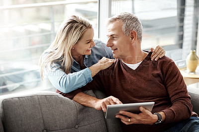 Buy stock photo Shot of a mature couple using a digital tablet while relaxing together on the sofa at home