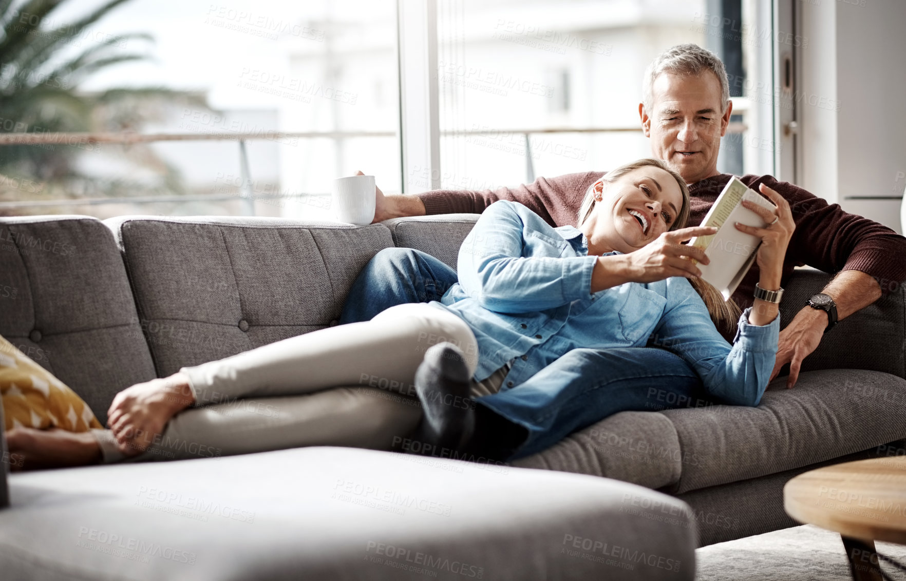 Buy stock photo Shot of a mature couple reading a book together while relaxing on the sofa at home