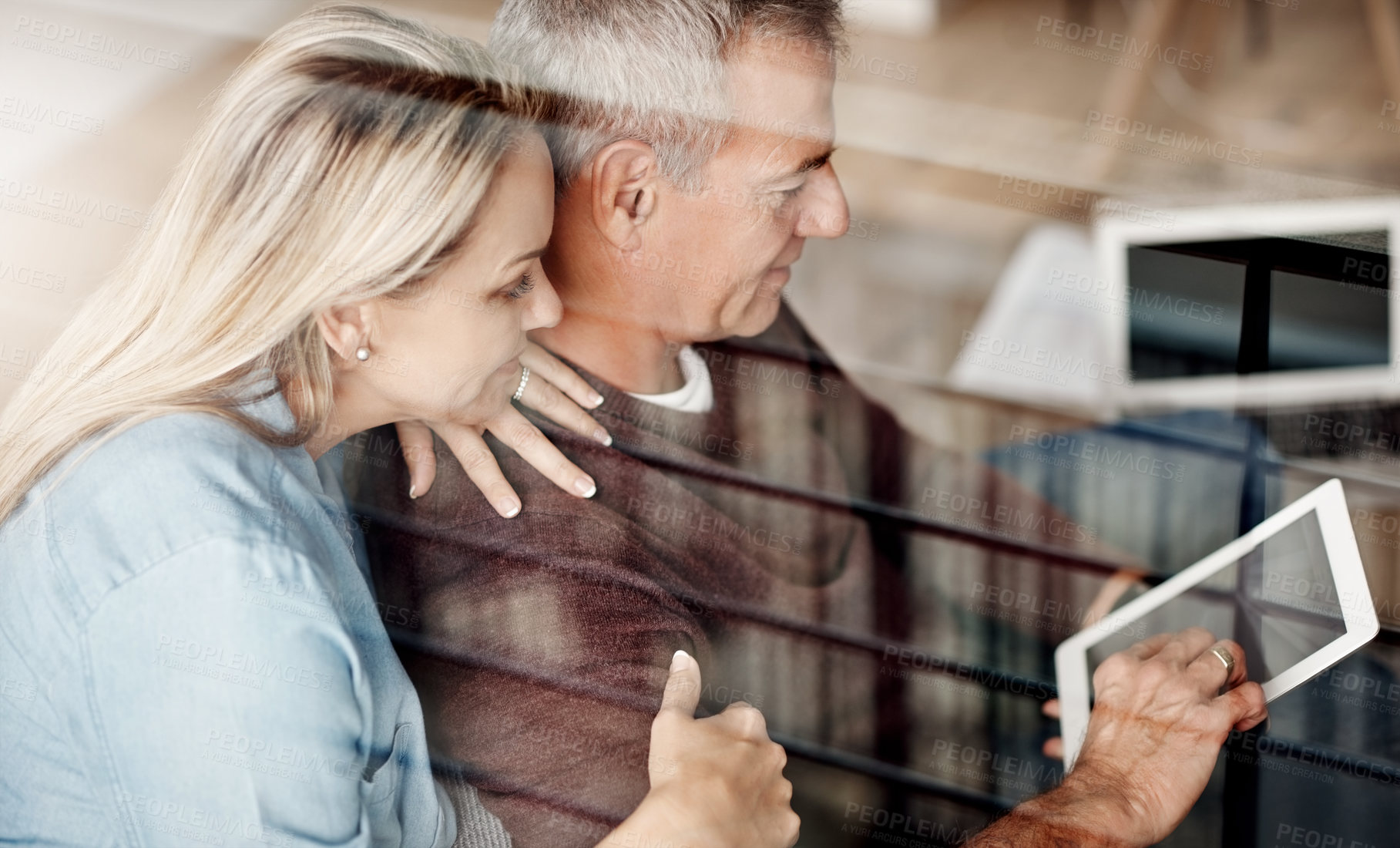 Buy stock photo Shot of a mature couple using a digital tablet while relaxing together on the sofa at home