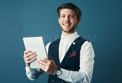 Buy stock photo Studio shot of a handsome young businessman using a tablet against a blue background