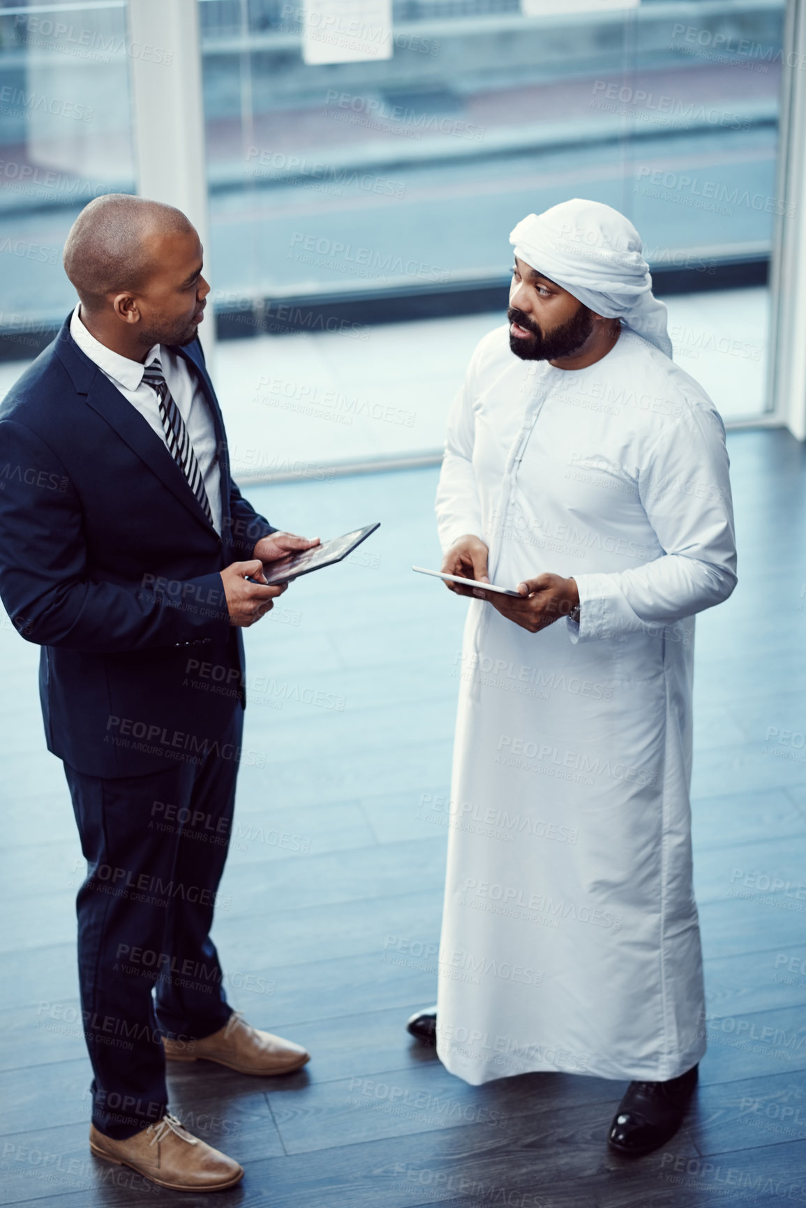 Buy stock photo Shot of two businessmen using digital tablets while having a discussion in a modern office