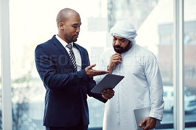 Buy stock photo Shot of two businessmen using a digital tablet while having a discussion in a modern office