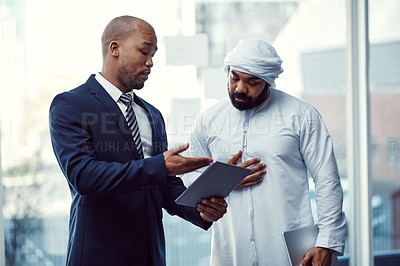 Buy stock photo Shot of two businessmen using a digital tablet while having a discussion in a modern office