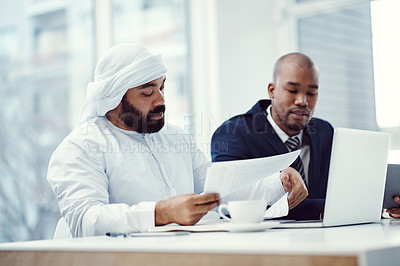 Buy stock photo Shot of two businessmen using a laptop while having a discussion over paperwork in a modern office