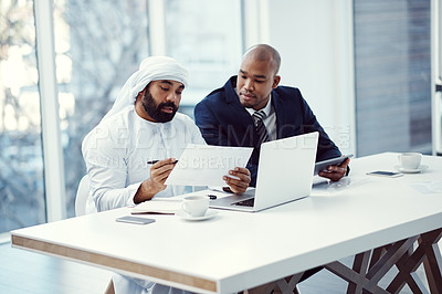 Buy stock photo Shot of two businessmen using a digital tablet and laptop while having a discussion in a modern office