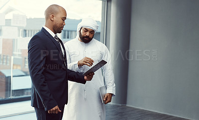 Buy stock photo Shot of two businessmen using a digital tablet while having a discussion in a modern office
