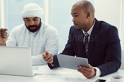 Buy stock photo Shot of two businessmen using a digital tablet and laptop while having a discussion in a modern office