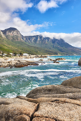 Buy stock photo Landscape view of ocean beach, sea, clouds, blue sky with copy space on Camps Bay, Cape Town, South Africa. Tidal waves washing on shoreline rocks or boulders. Background of Twelve Apostles mountains