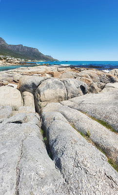 Buy stock photo Rocky landscape leading to the sea under cloudy blue sky copy space at Camps Bay beach, Cape Town, South Africa. Boulders on coastal shore with the Twelve Apostles mountain in the background