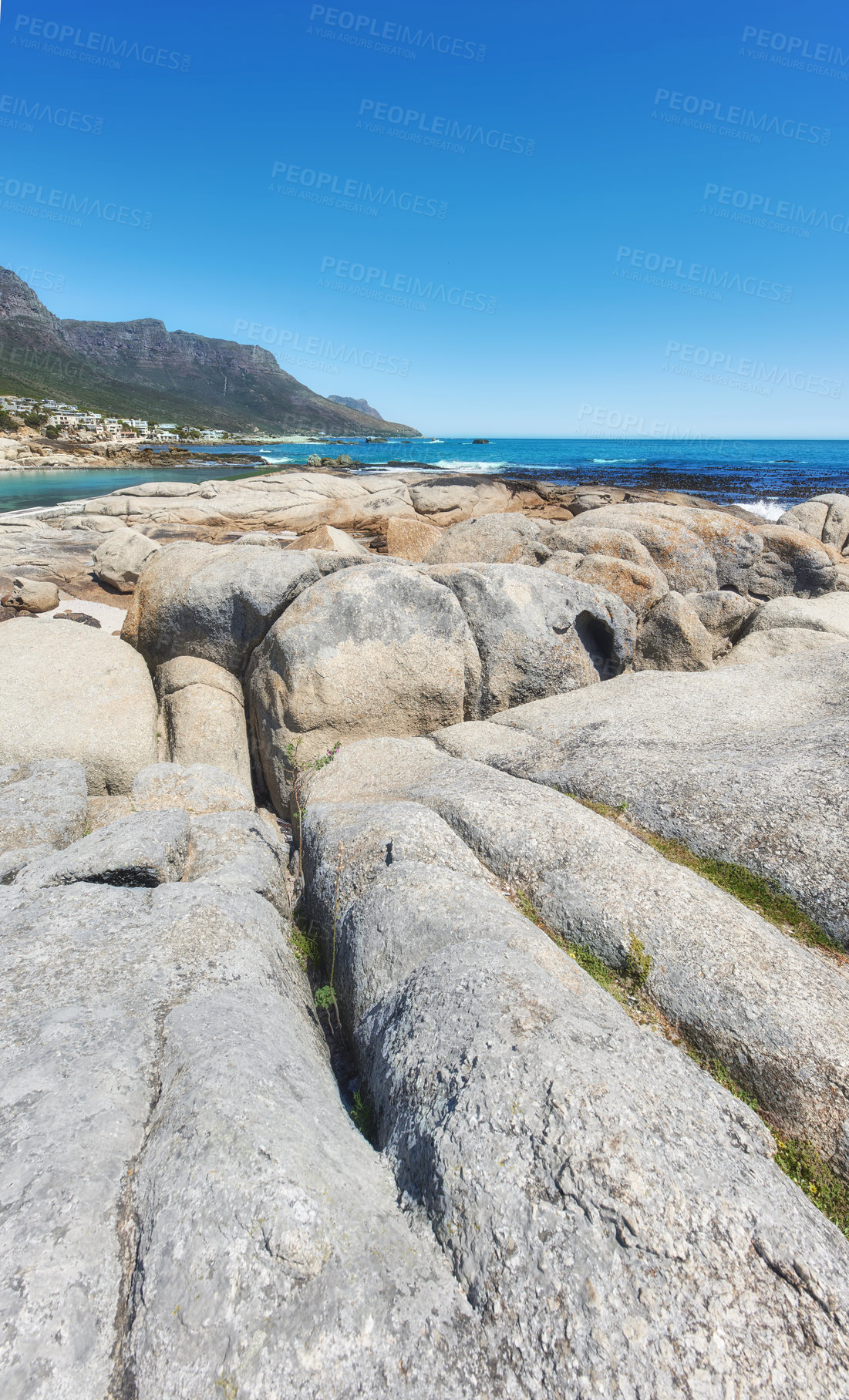 Buy stock photo Rocky landscape leading to the sea under cloudy blue sky copy space at Camps Bay beach, Cape Town, South Africa. Boulders on coastal shore with the Twelve Apostles mountain in the background