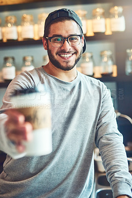Buy stock photo Portrait of a young barista holding a cup of coffee in a cafe