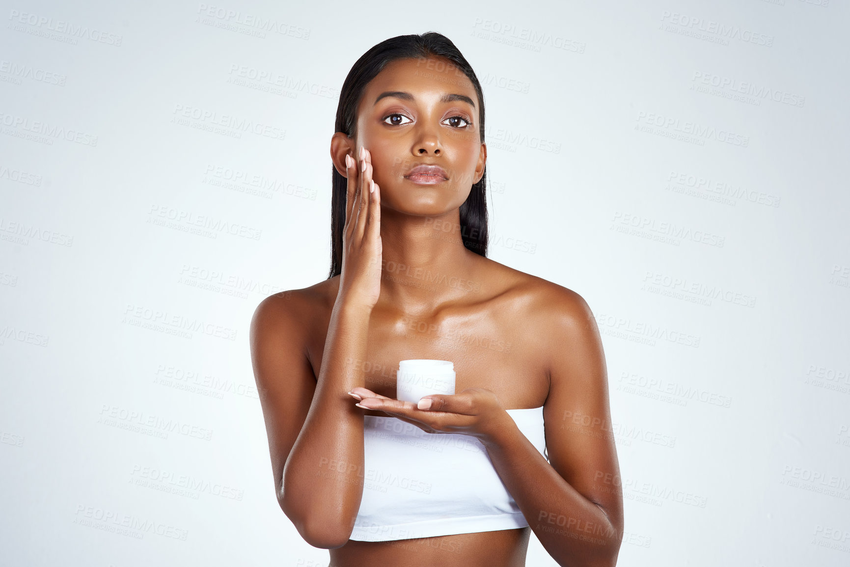 Buy stock photo Studio shot of a beautiful young woman applying moisturizer to her face against a light background