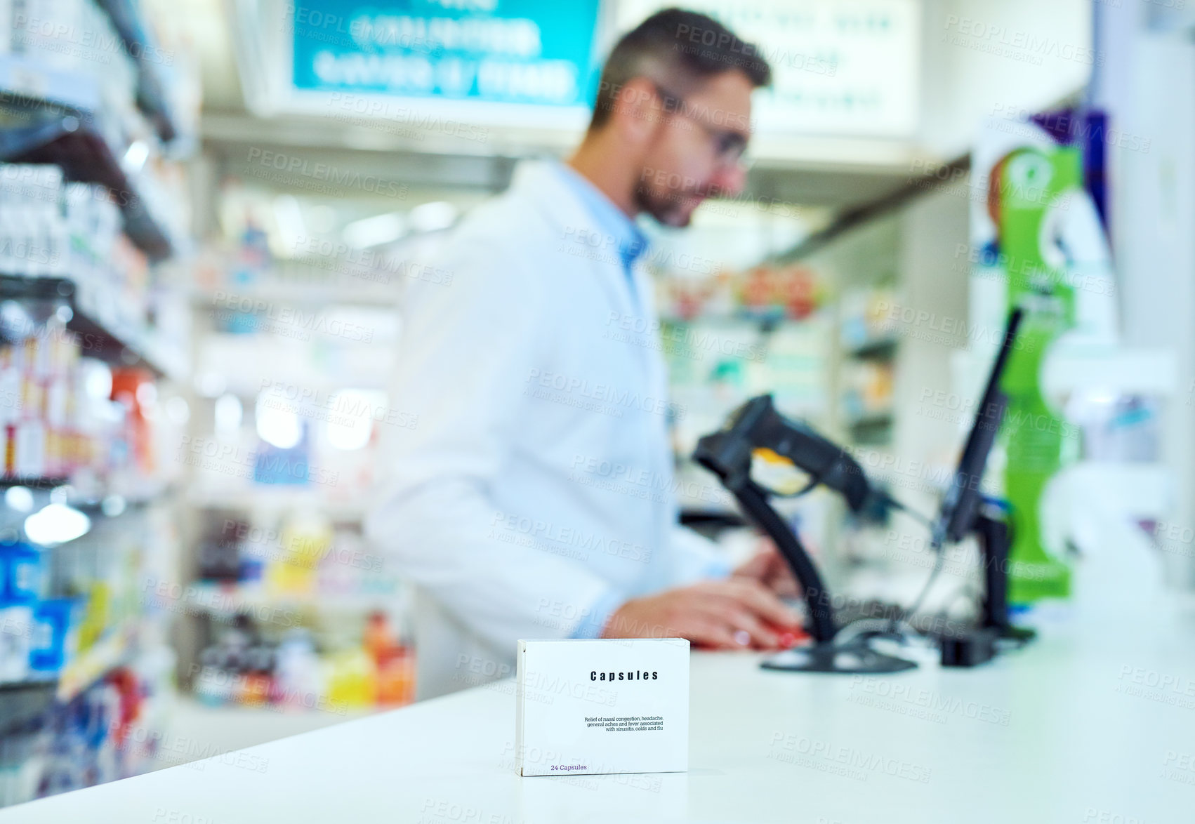 Buy stock photo Shot of a medicine package on the pharmacy counter while an unrecognizable male pharmacist works in the background