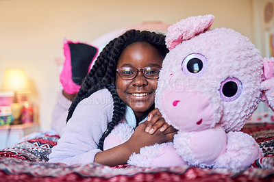 Buy stock photo Portrait of an adorable little girl holding a plush toy while lying on her bed in her bedroom