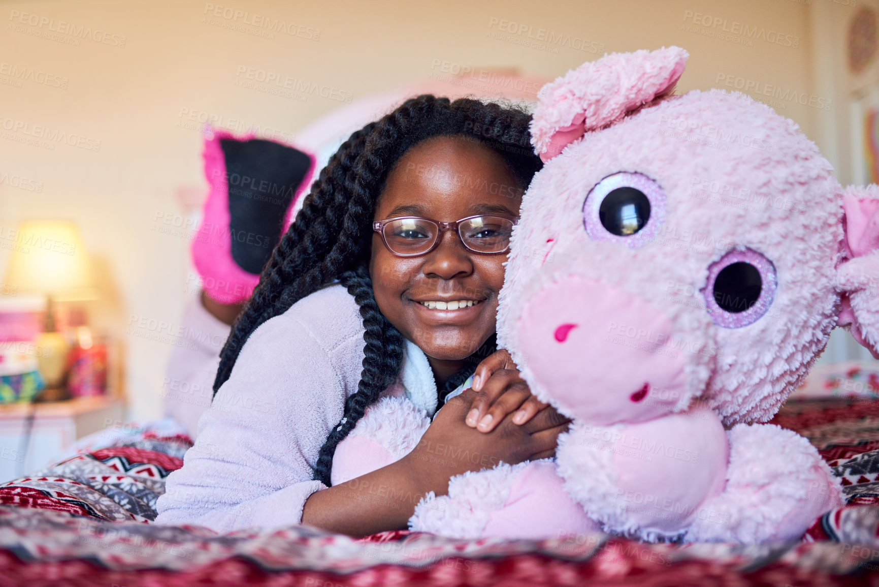Buy stock photo Portrait of an adorable little girl holding a plush toy while lying on her bed in her bedroom