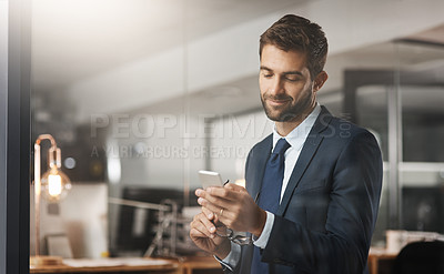 Buy stock photo Shot of a young businessman using a cellphone while working late in an office