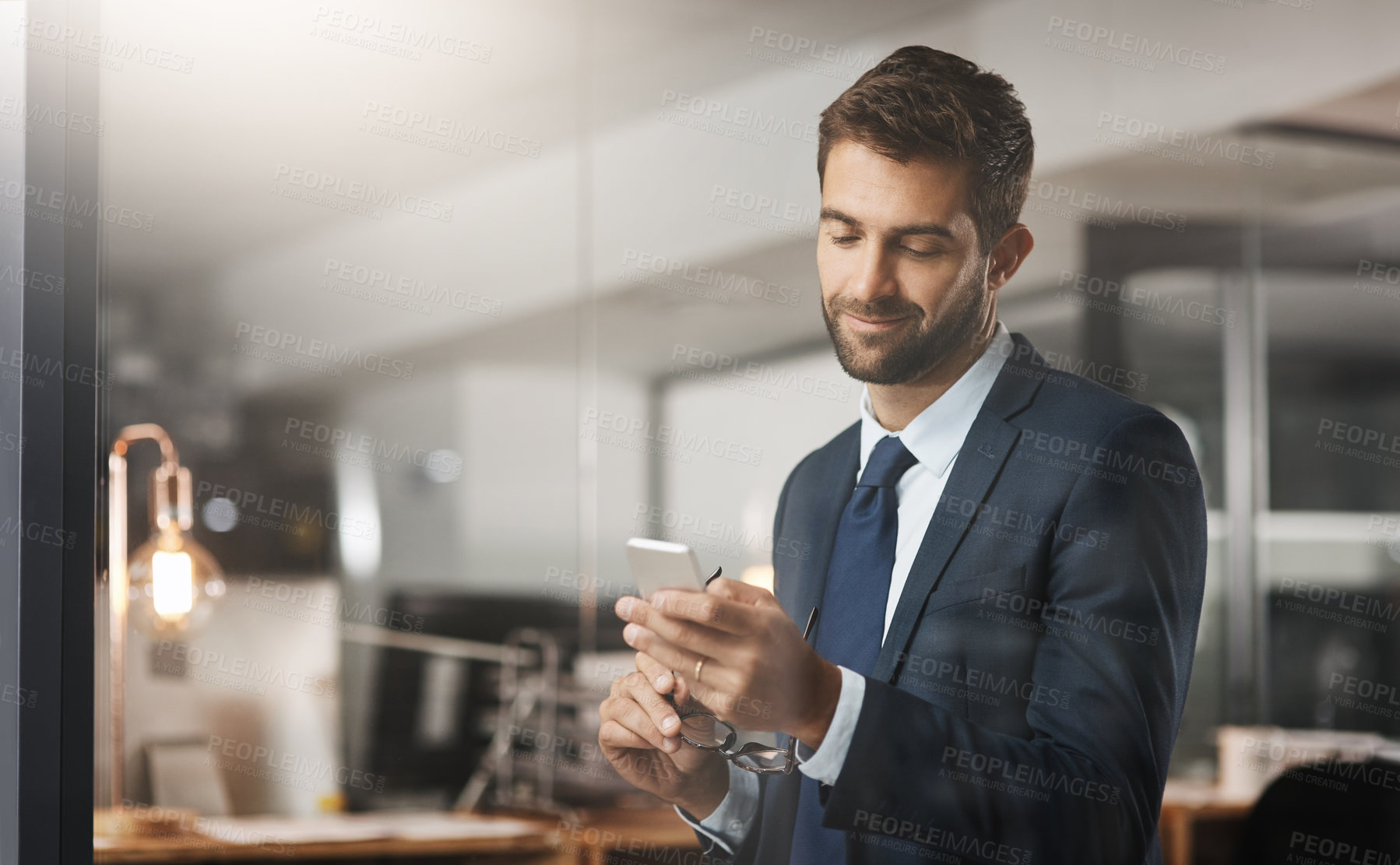 Buy stock photo Shot of a young businessman using a cellphone while working late in an office
