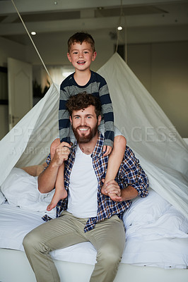 Buy stock photo Cropped portrait of a handsome young man sitting on the bed at home with his son on his shoulders