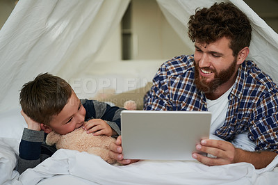 Buy stock photo Cropped shot of a handsome young man and his son using a tablet while lying on the bed at home