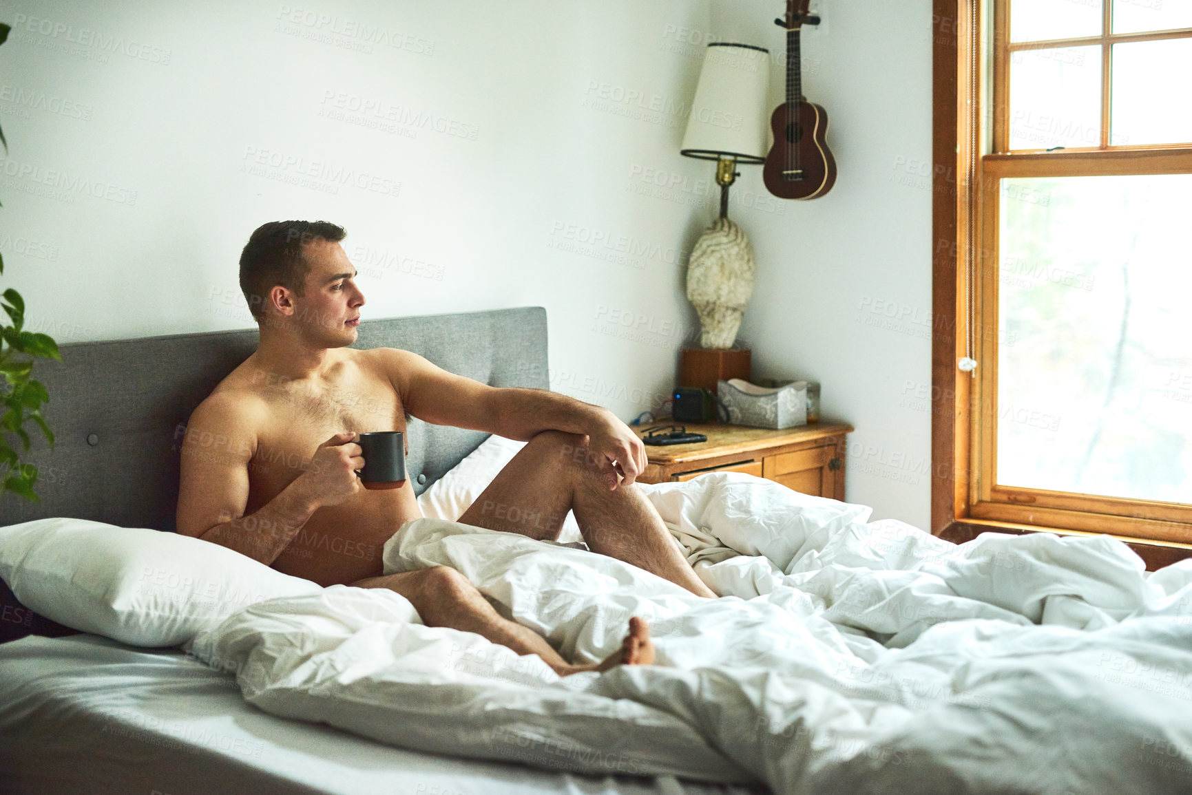 Buy stock photo Shot of a young handsome shirtless man drinking coffee and chilling in bed at home