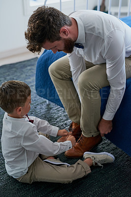 Buy stock photo Cropped shot of an adorable little boy tying his fathers shoelaces at home