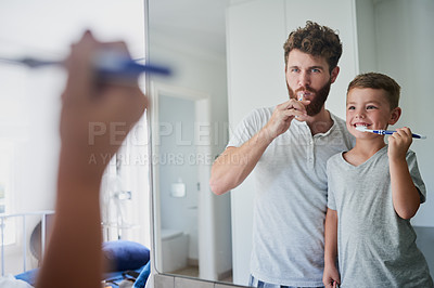 Buy stock photo Shot of a father and his little son brushing their teeth together in the bathroom at home