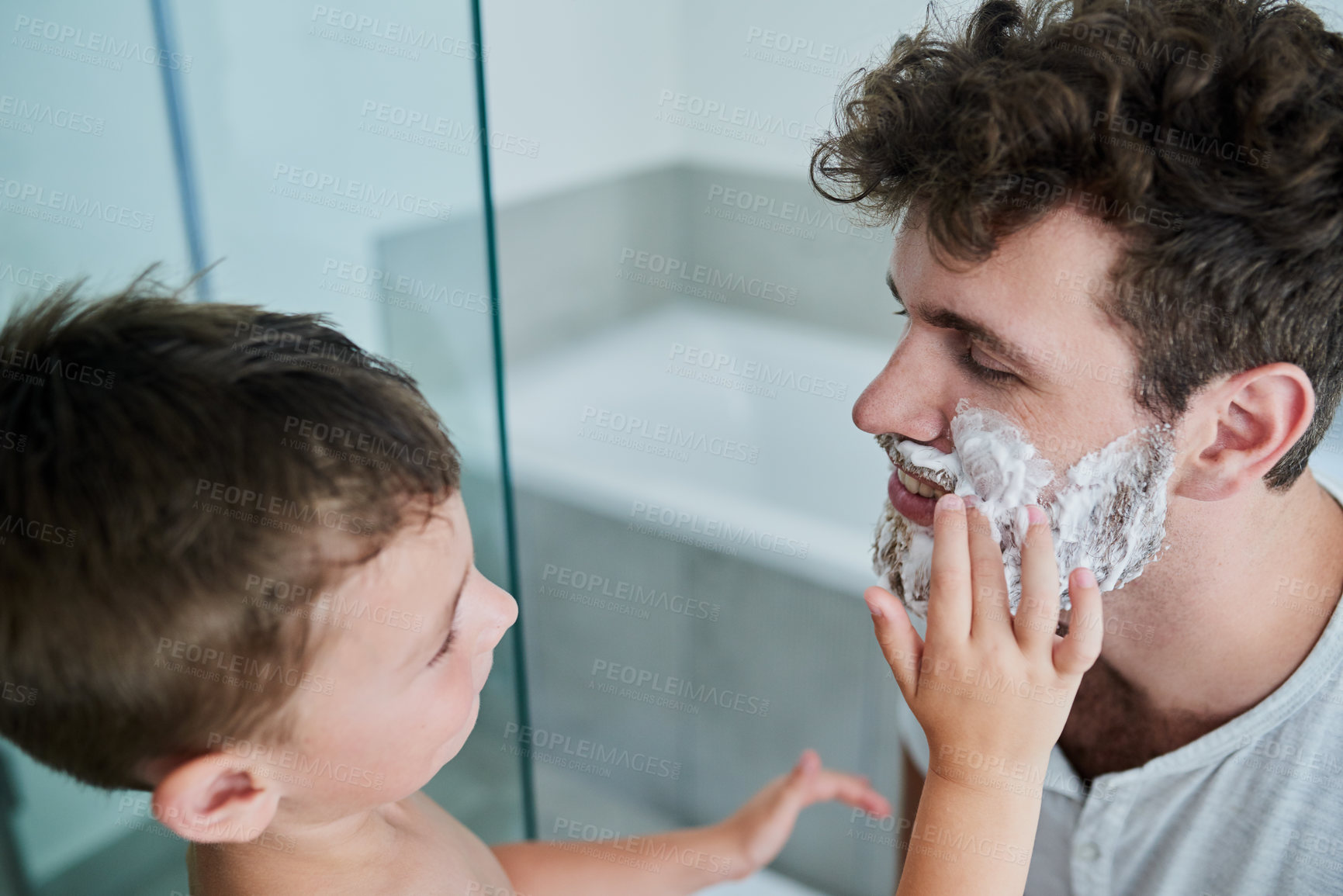 Buy stock photo Shot of a little boy rubbing shaving cream on his father's face in the bathroom at home
