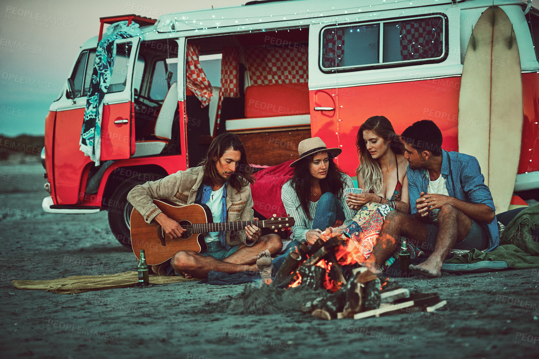 Buy stock photo Shot of a group of friends sitting around a fire on the beach