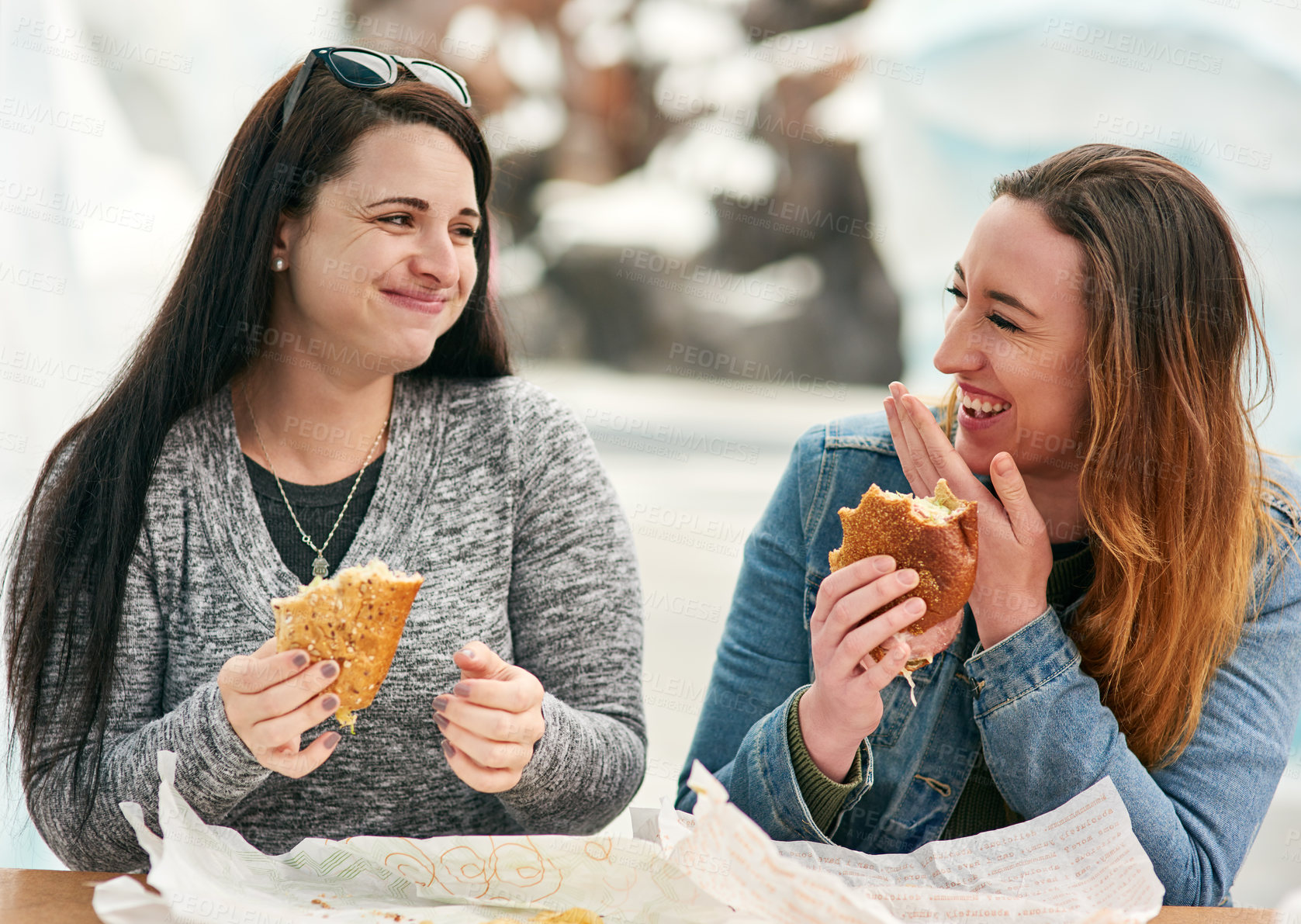 Buy stock photo Cropped shot of two female best friends eating sandwiches at an amusement park outside